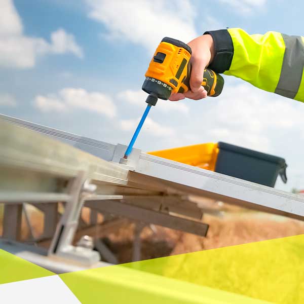 Nahaufnahme von einem Akkuschrauber der an einer Photovoltaik Halterung schraubt. Der Arm, der den Akkuschrauber hält, ragt von rechts in das Bild.