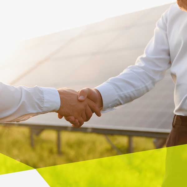 Zwei Personen mit weißen Hemden geben sich die Hand vor einer Solaranlage