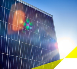 Solarpanel kommt von links ins Bild. Dahinter ist strahlender blauer Himmel und die Sonne blendet rechts hervor.