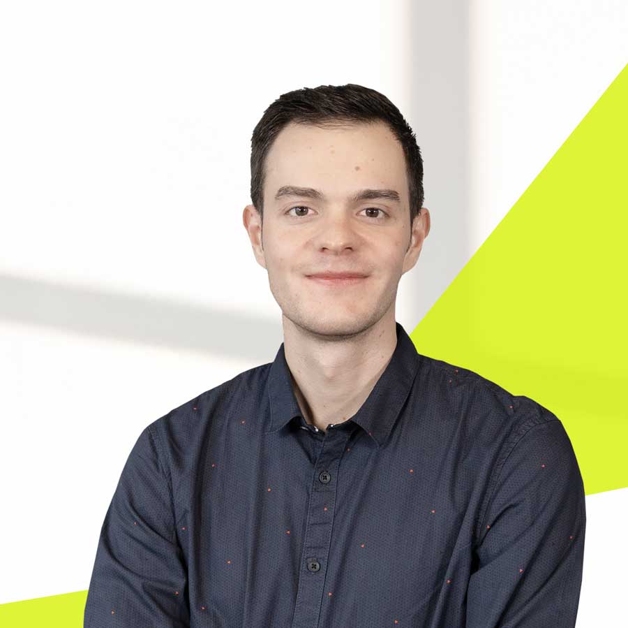 Johannes Liepert frontal, dunklaues Hemd mit roten kleinen Punkten blickt in die Kamera. Er hat eine sehr helle Haut, ohne Bart, markantes flaches Kinn und dunkles kurzes Haar.