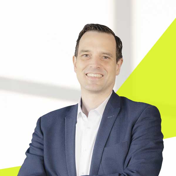 Olaf Timm, heller Raum mit grafischen hellgrünen Strahlen von links unten nach rechts oben und davor, Olaf im dunkelblauen Anzug, weißem Hemd, Lächeln mit Zähne und Kurzhaarschnitt.