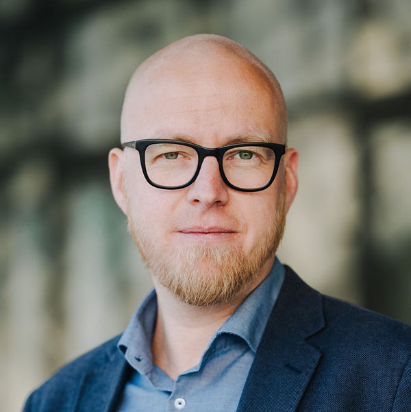 Konstantin Gastmann Zitatgeber steht vor einem verschwommenen grünlichen Hintergrund und trägt ein mittelblaues Hemd, dunkelblaues Jarkett